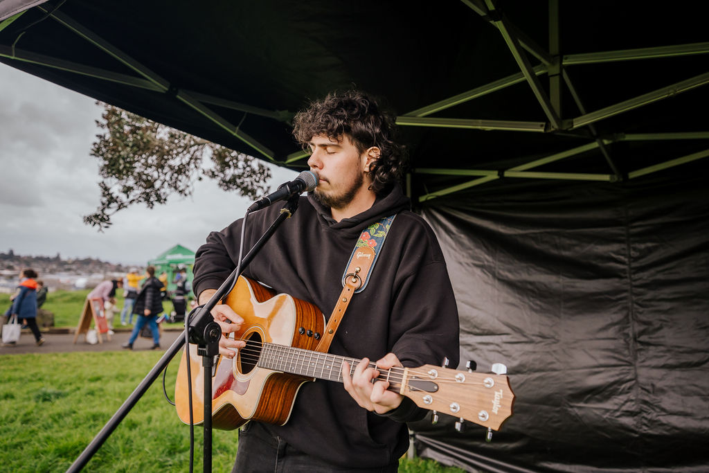 Youth musician playing guitar and singing on stage at an event.
